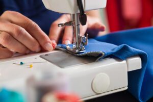 A close-up of a tailor’s hands as they sew a zipper onto a garment.
