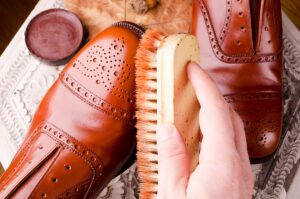 A person cleans and polishes a pair of brown dress shoes.